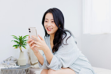 ベッドに座ってスマホを使っている女性