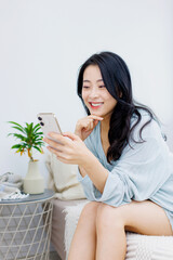 ベッドに座ってスマホを使っている女性