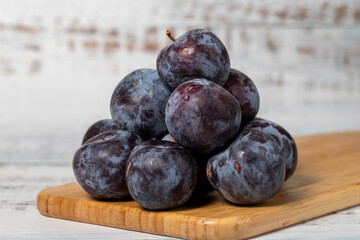 Fresh black plums on a white wooden background. Organic agricultural products. Delicious black plums