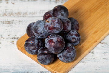 Fresh black plums on a white wooden background. Organic agricultural products. Delicious black plums