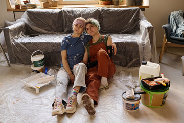 Obraz na płótnie Canvas Lesbian couple sitting on the floor and resting during repair in their new apartment