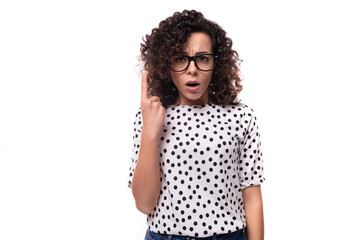 young caucasian businesswoman with curly hair dressed in a blouse with polka dots points her finger...