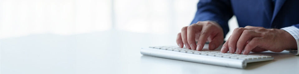 Businessman working on laptop PC computer at the desk in the office. Young man typing on computer keyboard Write an email or communicate online. Copy space, banner, panorama.