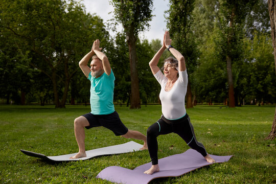 Active older couple doing yoga exercise outdoors at city park