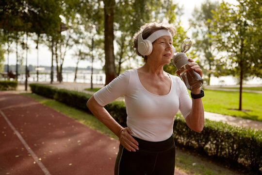 Elderly woman drinking water taking short break during running exercise