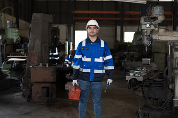 Portrait of male engineer worker working in factory, wearing safety uniform, helmet while holding equipment tools