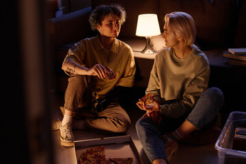 Lesbian couple eating pizza after move in the evening while sitting on the floor in their new...