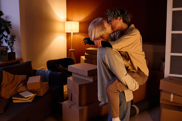 Young lesbian couple happy to move, they kissing among boxes in the room - obrazy, fototapety, plakaty