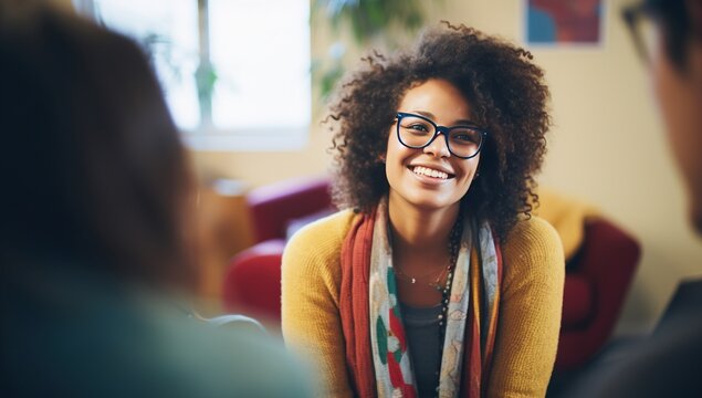Young Black adult woman with long curly hair, wearing glasses and a yellow cardigan, smiling, looking directly at the viewer.