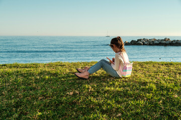 Naklejka na ściany i meble Playa de Pedregalejo, Málaga, niña seis años en el césped, frente al mar, escribiendo en su diario, día soleado, cielo sin nubes
