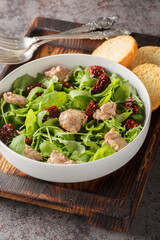 Cod liver salad with arugula and sun-dried tomatoes close-up in a bowl on the table. Vertical