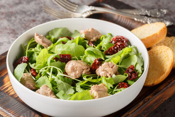 Delicious cod liver salad with arugula and sun-dried tomatoes served with toast close-up in a bowl on the table. Horizontal