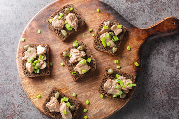 Homemade rye bread sandwiches with cod liver, capers and green onions close-up on a cutting board on the table. Horizontal top view from above