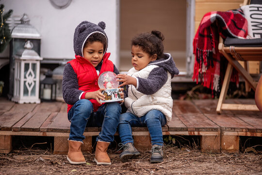African American boy and girl are sitting on wooden pallets, playing with a Christmas snow globe