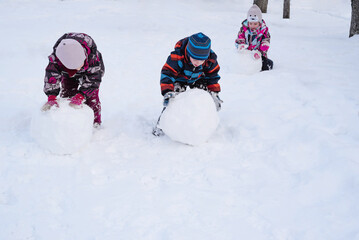 Happy children rolling a snow globe for a snowman. Children playing with snow. Winter entertainment...