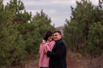 Close-up portrait of couple hugging in green coniferous forest. Young man tactilely wrapped woman