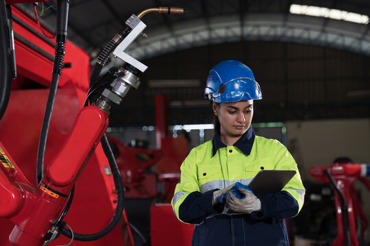 Female engineer inspecting quality and maintenance autonomous robotics arm system welding in factory