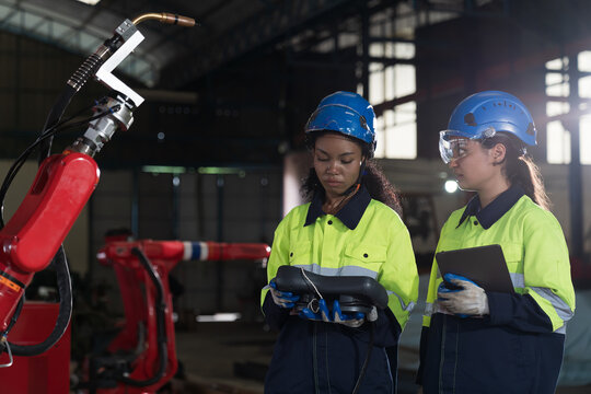 Team of female engineer inspecting quality of autonomous robotics arm. Group of technician maintenance and control robotics arm in factory - Powered by Adobe