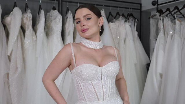 Portrait of a woman in a wedding dress looking at the camera in a boutique store. A seductive image of a brunette in a wedding dress. Wedding salon with a new collection of dresses. Wedding fashion.