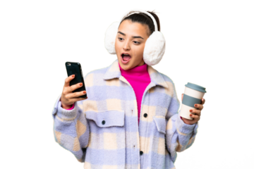 Young woman wearing winter muffs over isolated chroma key background holding coffee to take away and a mobile