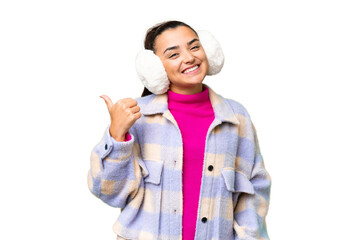 Young woman wearing winter muffs over isolated chroma key background pointing to the side to...