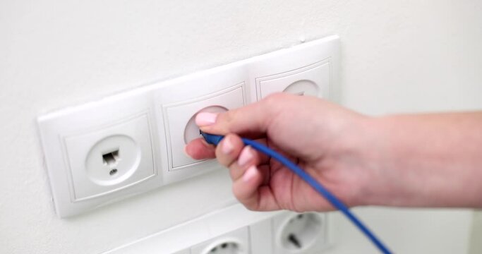 The hand includes the Internet cord in the outlet on the wall, close-up. Wall socket computer