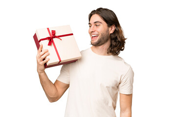 Young handsome man holding a gift over isolated background with happy expression