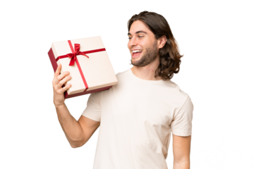 Young handsome man holding a gift over isolated background with happy expression