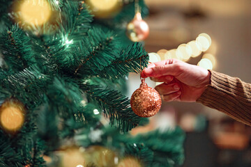 Close-up hand of woman decorating Christmas tree with baubles balls on the background of festive...