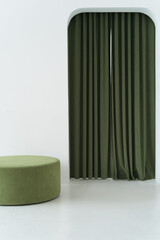 Part of a minimalist interior with a green ottoman and green curtains