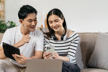 Young couple sitting on couch are using credit card payment through smartphone, buying furniture enter house, working on design together having conversation.