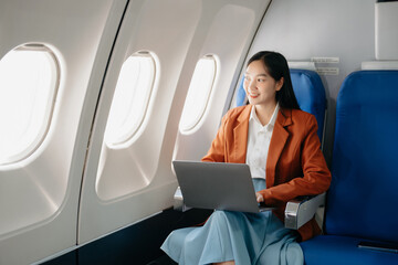 Attractive Asian female passenger of airplane sitting in comfortable seat while working laptop and tablet with mock up area using wireless connection.