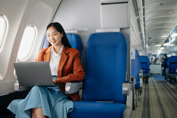 Young Asian executive excels in first class, multitasking with digital tablet, laptop and...