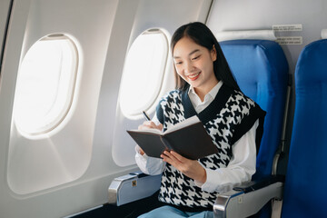 Young Asian executive excels in first class, multitasking with digital tablet, laptop and...