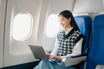 Attractive Asian female passenger of airplane sitting in comfortable seat while working laptop and...