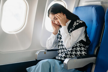 Photo of a frustrated woman sitting on an airplane with her head in her hands. woman sitting in a seat in airplane. - obrazy, fototapety, plakaty