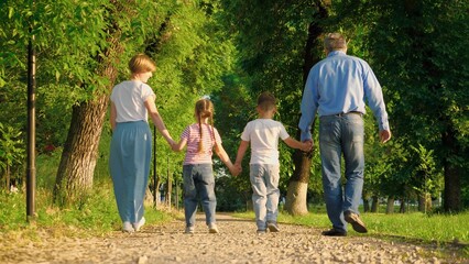 Small children walk with joint hands with pleased parents on park ground road