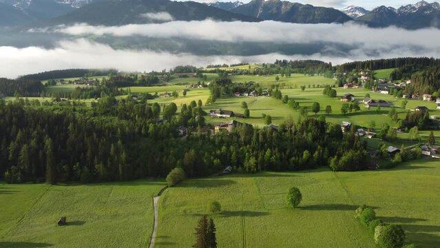 4K drone shot of beautiful misty sunrise at Ramsau am Dachstein, Styria, Austria. Lush green fields and guesthouses at the foot of Dachstein Glacier, popular area for Alpine skiing and snowboarding.