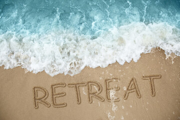 Word Retreat drawn on sand near sea, above view