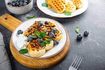 Homemade waffles with blueberries, chocolate sauce and cream cheese in a plate and a grey background