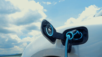 Electric car plug in with charging station, recharge battery by EV charger cable display smart digital battery status hologram with nature background. Futuristic green energy infrastructure.Peruse