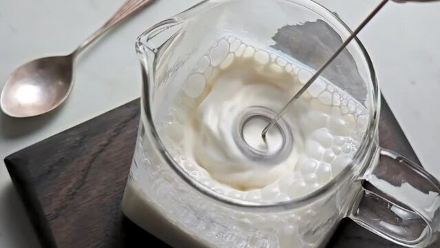 Ultra slow motion foaming of milk in a glass milk jug with an electric whisk