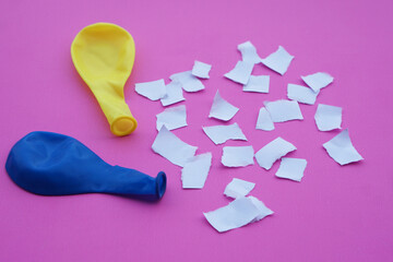 Blue and yellow balloons with no air, small pieces of paper. Pink background. Concept, equipment...