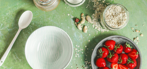 Healthy breakfast flat lay with bowl, spoon, strawberries,  oat flakes and nuts on green...