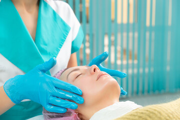 A female cosmetologist manually treats the patient's skin with a moisturizing and toning gel.