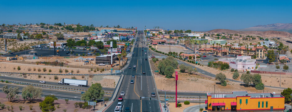 Aerial view of a bustling southwestern U.S. town, showcasing beige and brown buildings with terracotta roofs, amidst a clear, sunny desert landscape with a mountain backdrop. - Powered by Adobe