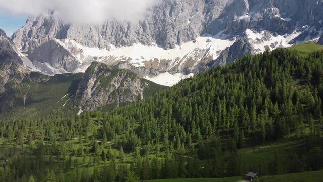 4K drone shot of majestic Dachstein Glacier, Styria, Austria in the Alps. Popular area for Alpine and cross-country skiing, snowboarding. Huge rock formations overlook lush green fields.