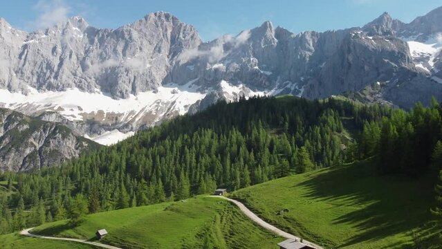 4K drone shot of majestic Dachstein Glacier, Styria, Austria in the Alps. Popular area for Alpine and cross-country skiing, snowboarding. Huge rock formations overlook lush green fields.
