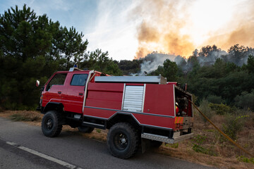 Carro dos bombeiros junto a uma estrada na luta de um incêndio florestal com grandes labaredas que...