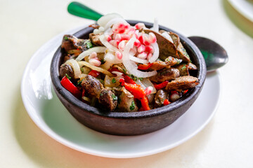 travel to Georgia - portion of Kuchmachi (Georgian dish of livers, hearts and gizzards with sliced fresh onion and pomegranate seeds for topping) in hot ceramic bowl on table in local cafe in Batumi